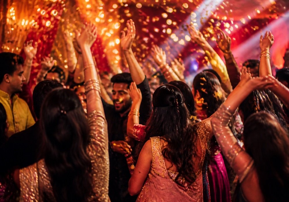 Guests dancing under gold lights and confetti at a Bollywood party