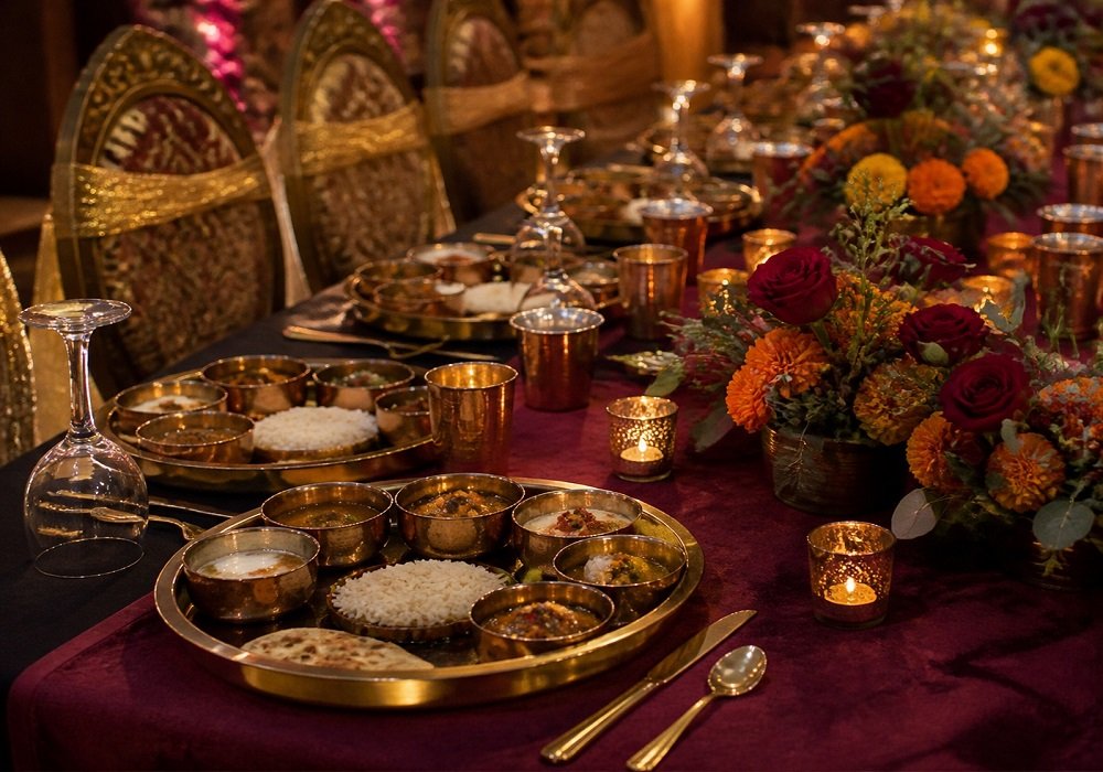 Bollywood theme table setting with brass thali, maroon runner and marigold centrepiece